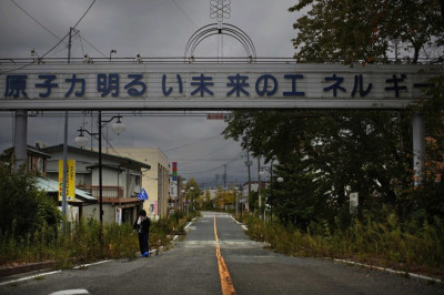 A woman who came for a brief visit to her home walks under a sign reading "Nuclear Power - The Energy for a Better Future", at the entrance of empty Futaba town, inside the exclusion zone in Fukushima prefecture